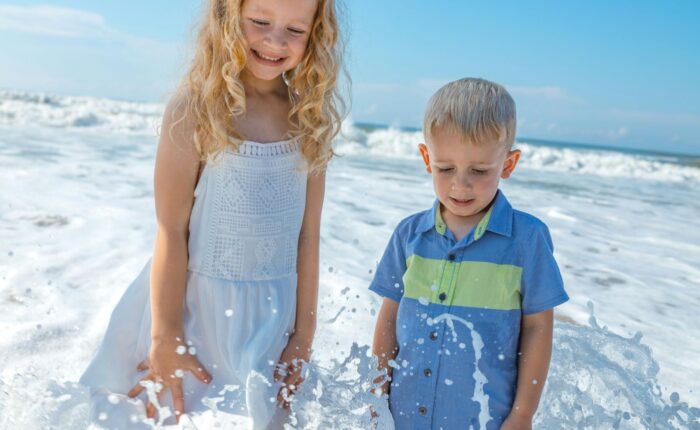 two blonde kids, likely brother and sister, hanging out at a beach