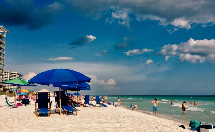 A beach with many people, beach chairs, and umbrellas