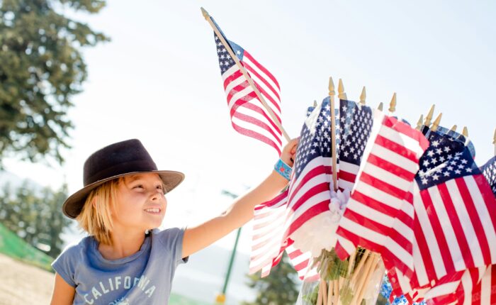 a kid in a blue shirt and brown hat reaching to several American flags