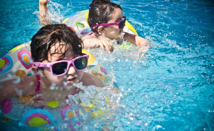 two kids with sunglasses in water wearing flotation devices