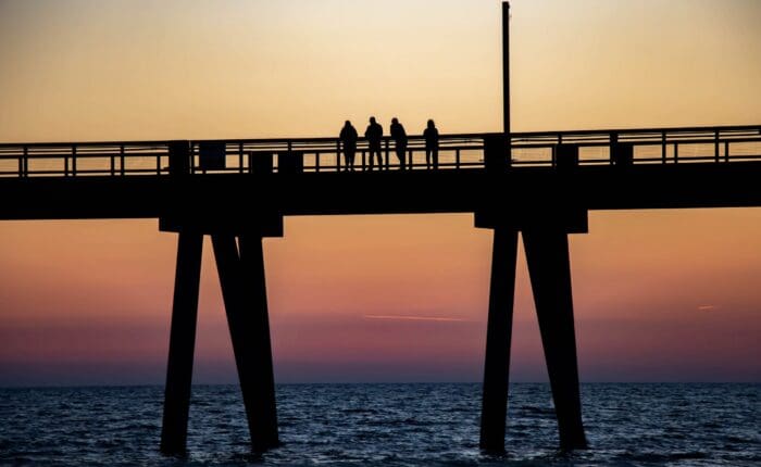 Four people stand on a pier at Crab Island, watching the sunset during a Dolphin Cruise.